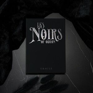 May include: A black box with silver lettering that reads "LES NOIRS OF ODILON" and the word "ORACLE" below. The box is on a dark surface with black accents.