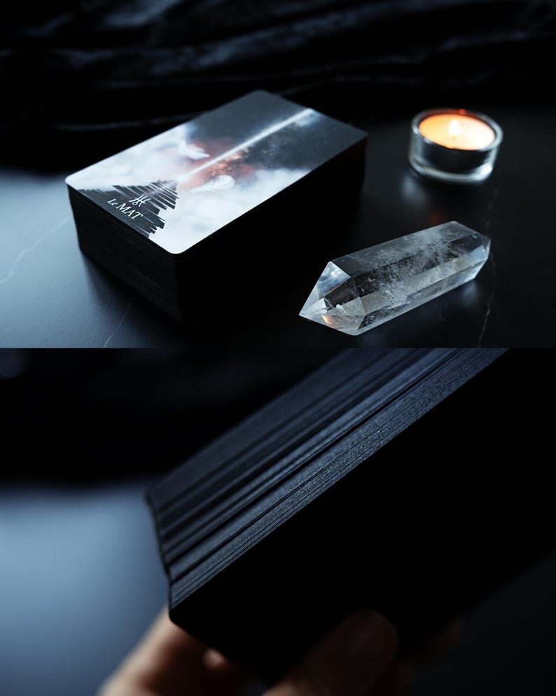 May include: A stack of black tarot cards with the text "LE MAT" on the top card. A clear quartz crystal and a lit candle are next to the cards. The top card features a stairway leading into a cloudy sky.