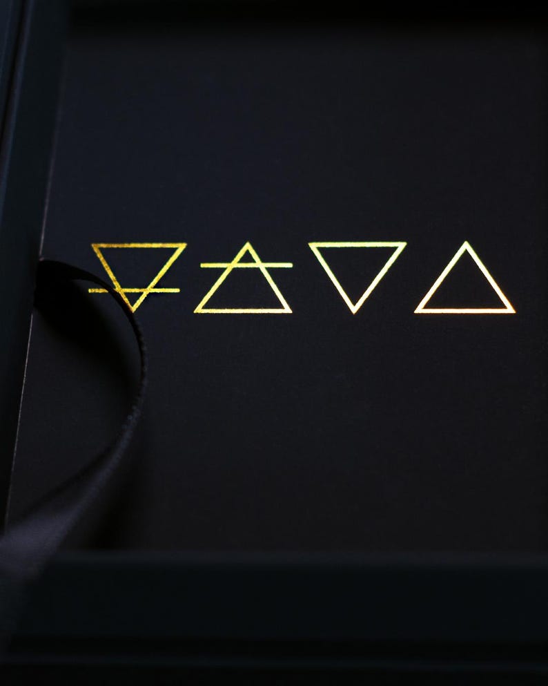May include: A black box with gold geometric symbols. The symbols include a line with a downward-facing triangle, a triangle with a horizontal line, an inverted triangle, and a triangle. The symbols are arranged in a row.