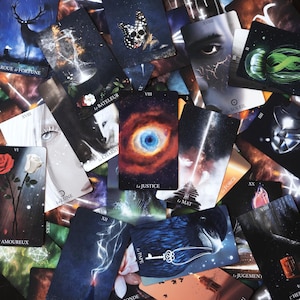 May include: A collection of tarot cards with various mystical illustrations. The cards feature images of a deer, a butterfly skull, an eye, and other symbolic imagery. Some cards have French text, including "La Justice" and "Le Monde."