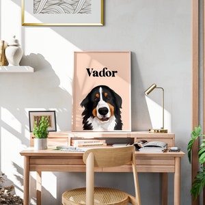 May include: A framed print of a Bernese Mountain Dog with the name "Vador" printed in black text on a light pink background. The print is hanging above a wooden desk with a chair and a lamp.