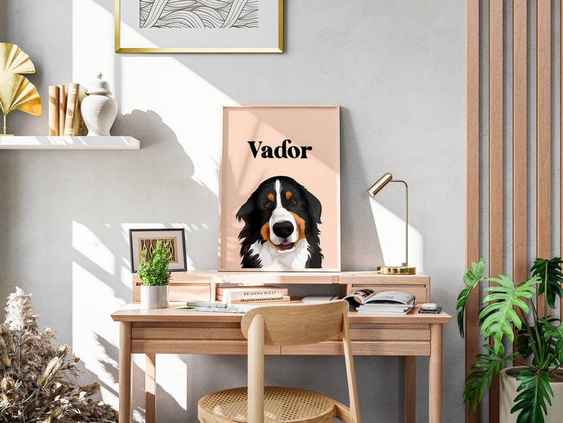 May include: A framed print of a Bernese Mountain Dog with the name "Vador" printed in black text on a light pink background. The print is hanging above a wooden desk with a chair and a lamp.