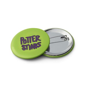 Könnte beinhalten: Ein grüner Knopf mit dem Text "Potter Stinks" in lila Schrift.