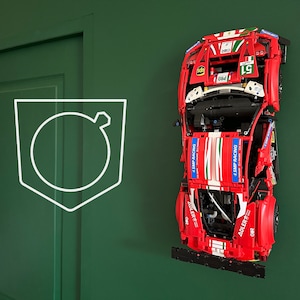 Peut inclure: Un modèle de voiture de course Lego Ferrari 488 GTE rouge, blanc et vert avec le texte "SMP Racing" et "ADLER" sur les côtés. La voiture est à l'envers et montée sur un mur.