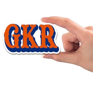 May include: A sticker with the letters "GKR" in a retro style. The letters are orange with a blue outline and a white border.