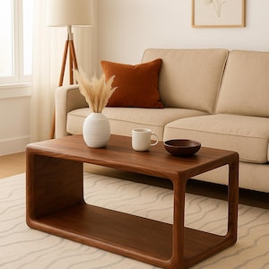 May include: A rectangular dark wood coffee table with rounded corners and an open lower shelf. On the table sits a white ribbed vase containing dried pampas grass, a plain white ceramic mug, and a small dark brown wooden bowl.