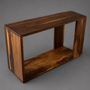May include: A rectangular console table constructed from dark brown wood with a visible natural grain pattern. The piece features a hollow, open-frame design with a flat top surface, two vertical side panels, and a flat bottom base.