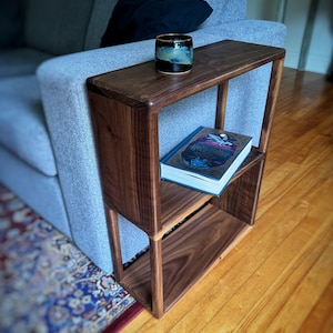 Puede incluir: Una mesa auxiliar de madera oscura con dos estantes, un libro titulado "Harry Potter y la Orden del F&eacute;nix" en el estante superior y una taza de cer&aacute;mica azul oscuro en la superficie superior.