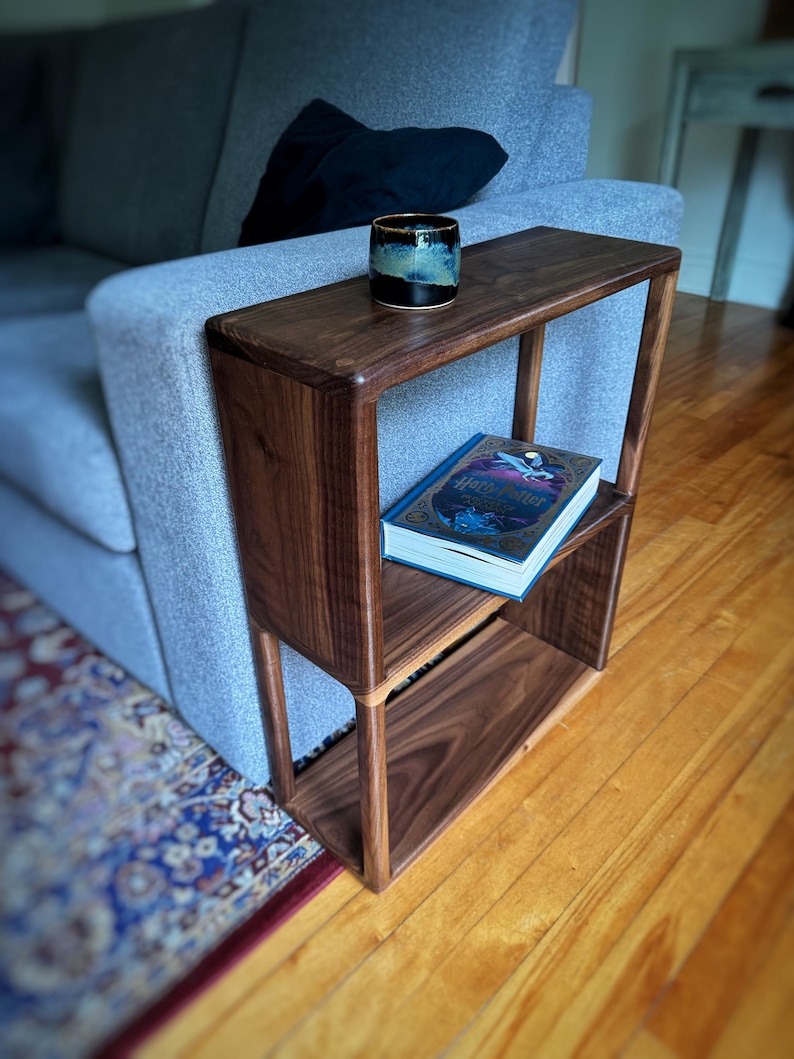 Puede incluir: Una mesa auxiliar de madera oscura con dos estantes, un libro titulado "Harry Potter y la Orden del F&eacute;nix" en el estante superior y una taza de cer&aacute;mica azul oscuro en la superficie superior.