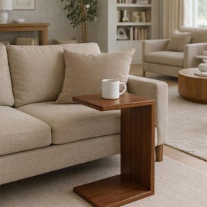 May include: A C-shaped side table made of dark brown wood with a smooth, flat surface. The table features a solid, continuous frame that curves to form a base and a tabletop, currently holding a plain white ceramic mug filled with a dark beverage.