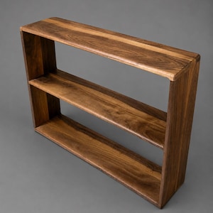 May include: A rectangular wall shelf crafted from dark brown wood with a visible natural grain pattern. The shelf features a single horizontal middle divider, creating two open storage compartments within the solid wooden frame structure.
