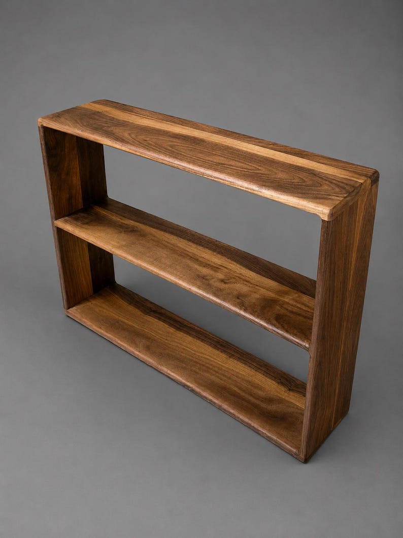 May include: A rectangular wall shelf crafted from dark brown wood with a visible natural grain pattern. The shelf features a single horizontal middle divider, creating two open storage compartments within the solid wooden frame structure.