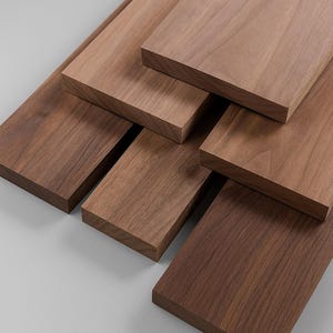 May include: A collection of rectangular wooden planks in varying shades of brown. The planks are arranged in a layered pattern, showcasing the natural wood grain and texture. The wood appears to be smooth and well-finished, suitable for woodworking projects.