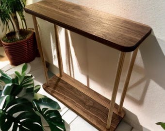 May include: A wooden console table with a dark brown top and bottom shelf, supported by light-colored, angled legs. The table is approximately 36 inches long, 12 inches wide, and 30 inches tall. The design is minimalist and modern, suitable for entryways or living rooms.