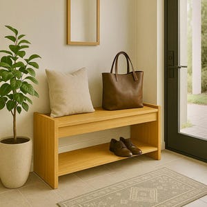 May include: A wooden bench with a lower shelf, featuring a tan cushion, a brown leather tote bag, and brown leather shoes. A rectangular mirror is mounted on the wall above. A potted plant and patterned rug complete the hallway scene.