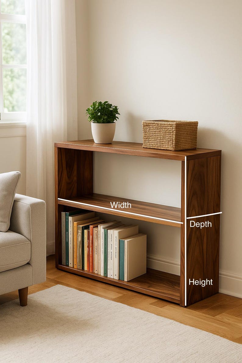 May include: A rectangular wooden bookshelf with two open shelves, featuring a dark brown wood grain finish. The unit displays white lines indicating width, depth, and height dimensions. The bottom shelf contains a row of books, while the top shelf holds a small potted green plant and a woven rectangular basket.