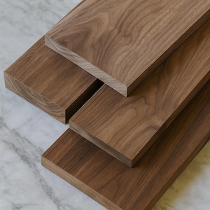 May include: Four rectangular wooden planks with a rich, dark brown color and visible wood grain are arranged on a white and gray marble surface. The planks are stacked at different angles, showcasing their natural texture.