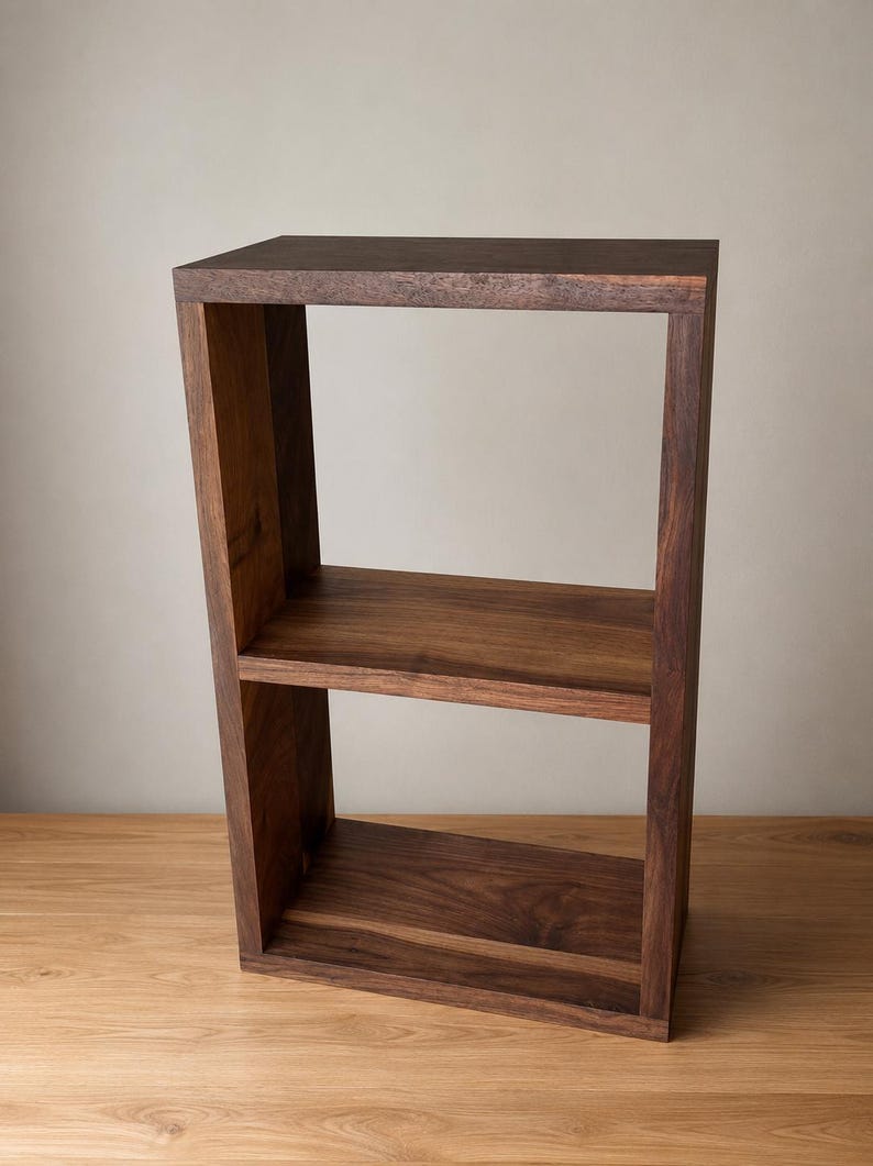 May include: A rectangular dark brown wooden shelf unit featuring a single horizontal middle shelf that divides the frame into two open storage compartments. The structure is constructed from solid wood with a visible grain pattern throughout the frame.