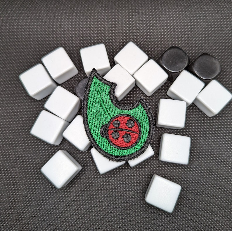 May include: A green leaf-shaped patch with a red ladybug in the center. The patch is surrounded by white square tiles.