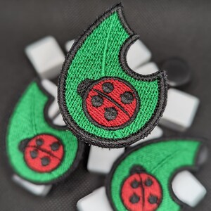 May include: Three green felt patches with a red ladybug design. The ladybugs have black spots and a black line down the middle. The patches are shaped like a leaf, a half-circle, and a full circle.