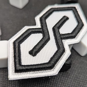 Peut inclure: Écusson brodé avec le design "S" emblématique en fil noir sur fond blanc. Le patch a une bordure blanche et une forme géométrique. Idéal pour les vêtements et accessoires.