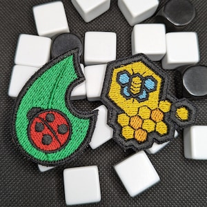 May include: Two embroidered iron-on patches. One is green with a red ladybug and the other is yellow with a blue bee and honeycomb.