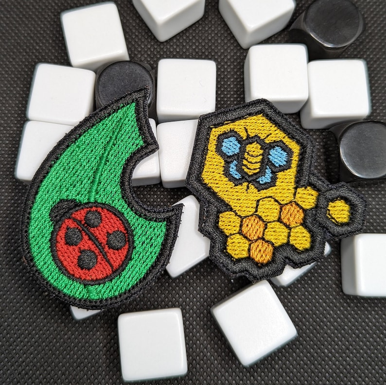 May include: Two embroidered iron-on patches. One is green with a red ladybug and the other is yellow with a blue bee and honeycomb.