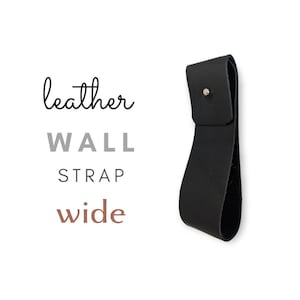 Op de afbeelding: Zwarte leren wandband met een brede lus en een zilveren klinknagel. De band heeft de tekst "leather wall strap wide".