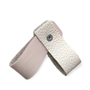 May include: A light beige leather handle with a metal screw in the center. The handle is designed to be attached to a bag or other object.