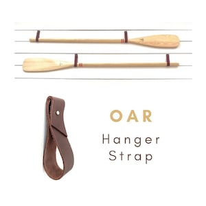 May include: Two wooden oars with red and white stripes hanging on a wall with a brown leather strap hanger labeled "OAR Hanger Strap".
