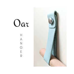 May include: A light blue leather hanger with a silver button. The hanger is attached to a wooden dowel.