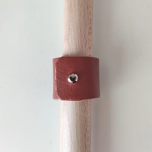 Op de afbeelding: Een bruin leren band met een zilveren knoop is om een houten pen gewikkeld.