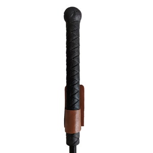 May include: A black leather riding crop with a braided handle and a brown leather strap.