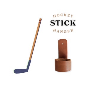 May include: A brown leather hockey stick hanger with the text "HOCKEY STICK HANGER" above it. The hanger is designed to hold a hockey stick upright.
