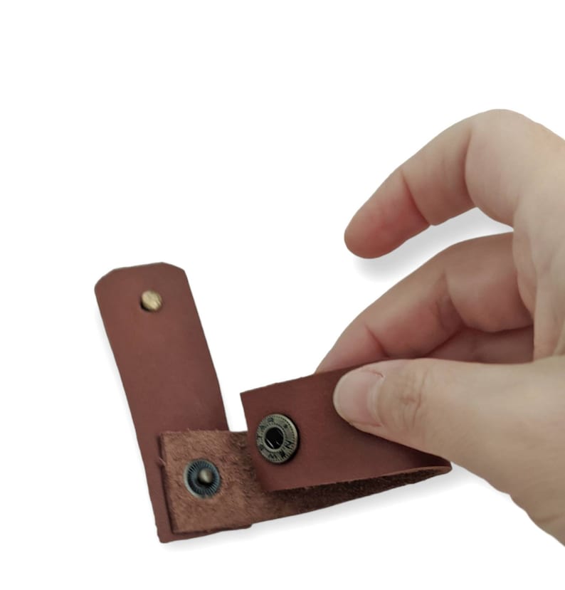 May include: A brown leather strap with two metal snaps. The strap is folded in half and the snaps are visible.