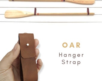 May include: Brown leather oar hanger strap with a metal button. The strap is designed to hang an oar on a wall.