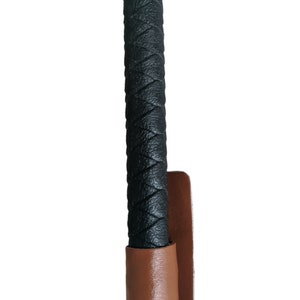 May include: Black leather riding crop with a brown leather grip and strap.