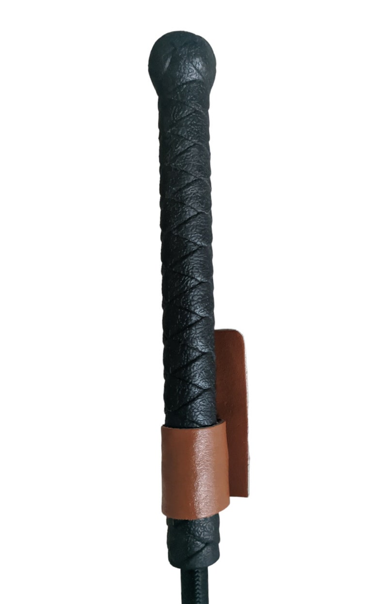 May include: Black leather riding crop with a brown leather grip and strap.