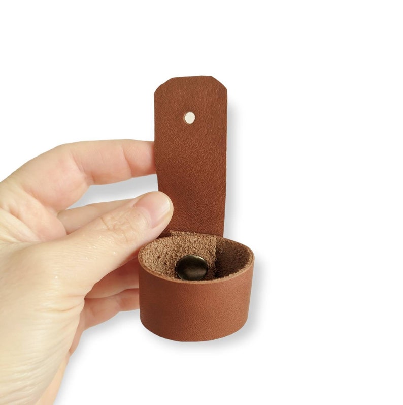May include: A brown leather strap with a hole and a snap closure. The strap is folded in half to show the inside of the strap.