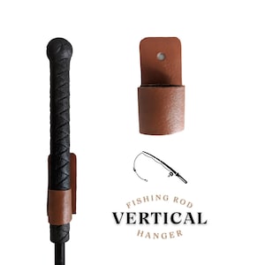 May include: A brown leather vertical fishing rod hanger with a black fishing rod in it. The hanger has a hole at the top for hanging on a wall. The text "Fishing Rod Vertical Hanger" is printed below the hanger.