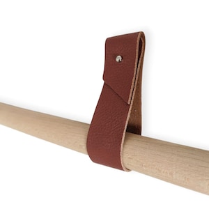 May include: A brown leather strap with a metal rivet, attached to a wooden dowel rod.