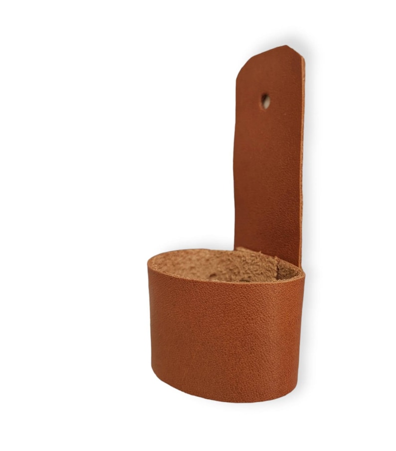 May include: A brown leather belt loop with a hole for a belt. The loop is designed to be attached to a belt and can be used to hold a variety of items, such as keys, a phone, or a wallet.
