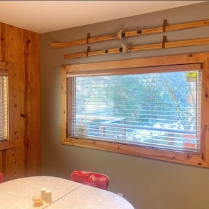 Peut inclure: Une table &agrave; manger en bois avec une surface blanche et deux chaises rouges. La table est &eacute;quip&eacute;e d'un set de sel et de poivre. La pi&egrave;ce a un mur en bois et une fen&ecirc;tre avec des stores. Il y a deux paires de skis accroch&eacute;s au mur.