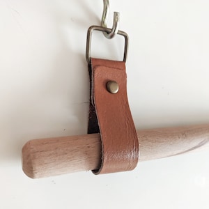 May include: A brown leather strap with a metal buckle and a brass rivet is attached to a wooden dowel rod.