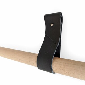 Könnte beinhalten: Schwarzes Lederband mit einem Metallnieten, befestigt an einer Holzstange.