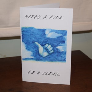 May include: A white card with blue watercolour artwork of a hand giving a thumbs up, with the text "Hitch a ride... on a cloud..."