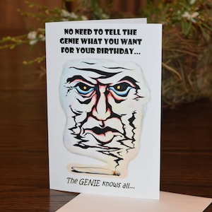 May include: A white greeting card with a cartoon genie face and a lit cigarette. The text on the card reads "NO NEED TO TELL THE GENIE WHAT YOU WANT FOR YOUR BIRTHDAY... The GENIE knows all..."