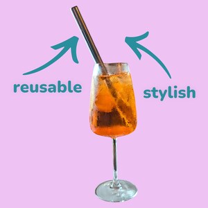 May include: A glass of orange juice with ice and a reusable metal straw. The straw is labeled "reusable" and the drink is labeled "stylish".