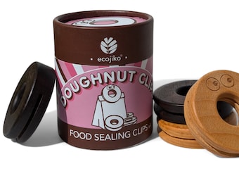 May include: A brown cardboard tube with a pink and white label that says "Doughnut Clips Food Sealing Clips" and a logo that says "ecojiko". The tube contains a set of wooden doughnut-shaped clips in brown and natural wood.