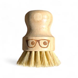 May include: A wooden brush with a natural bristle head and a bamboo handle. The handle has a face with glasses carved into it.